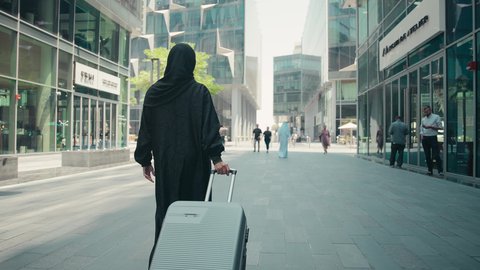 سيدة سعودية تستعد لبدء العطلة خارج البلاد , السياحة في إجازة الصيف, قضاء رحلة صيفية ممتعة, تصويرمن الخلف لشابة عربية خليجية اماراتية محجبة ترتدي العباءة تمسك بيدها حقيبة السفر بإيماءات السرور، الاستمتاع بجمال الطبيعة