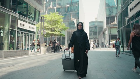 سيدة سعودية تستعد لبدء العطلة خارج البلاد , السياحة في إجازة الصيف, قضاء رحلة صيفية ممتعة, تصوير لشابة عربية خليجية اماراتية محجبة ترتدي العباءة تمسك بيدها حقيبة السفر بإيماءات السرور، الاستمتاع بجمال الطبيعة