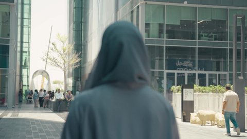 Interest in fashion, beauty and elegance, a photo from the back of a young Arab Gulf Emirati woman wearing an abaya and hijab, carrying shopping bags, taking advantage of seasonal discounts, buying women's clothes and accessories, modern Gulf women's abayas, a Saudi woman enjoying the pleasure of shopping