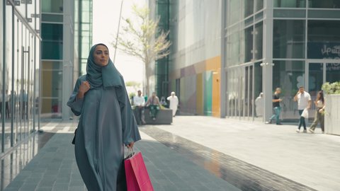 تصوير لشابة عربية خليجية اماراتية ترتدي العباءة والحجاب ، تحمل اكياس التسوق ، الاستفادة من التخفيضات الموسمية، عباءات خليجيه نسائيه عصريه، الإهتمام بالموضة والجمال والأناقة، شراء الملابس و الاكسسوارات النسائيه ، سيدة سعودية تستمتع بمتعة الشراء