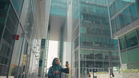 سيدة اماراتية تنظر بتعابير السرور تقوم باستخدام الهاتف المحمول ، استخدام الجوال والتقنيات الحديثه، اجراء مكالمة فيديو ،توثيق اللحظات السعيدة، امرأة عربية خليجية سعودية ترتدي العباءة والحجاب، نزهة وجولة فى الهواء الطلق