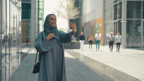 توثيق اللحظات السعيدة، استخدام الهاتف المحمول والتقنيات الحديثه، اجراء مكالمة فيديو ، امرأة عربية خليجية سعودية ترتدي العباءة والحجاب، سيدة اماراتية تنظر بتعابير السرور تقوم باستخدام الهاتف المحمول ، نزهة وجولة فى الهواء الطلق