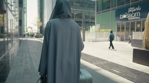 Enjoying the beauty of nature, a Saudi woman preparing to start her vacation abroad, summer vacation tourism, spending a pleasant summer trip, a photo from behind of a veiled young Arab Gulf Emirati woman wearing an abaya holding her travel bag with gestures of pleasure