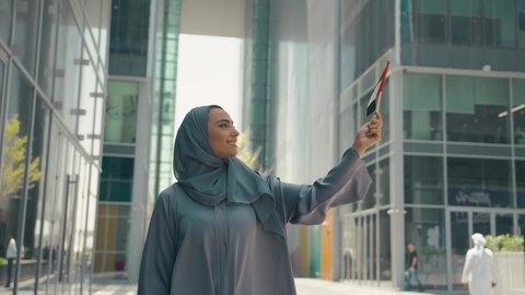 The concept of patriotism, UAE Independence Day, UAE National Day, UAE National Day celebration, a picture of an Emirati Gulf Arab woman wearing an abaya and hijab, holding the UAE flag