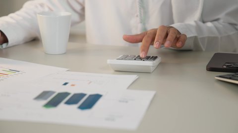 تناول القهوة الساخنة، وظيفة مكتبية في شركات الامارات العربية المتحدة، تحليل نتائج البيانات الاحصائية، تصوير مقرب لرجل عربي خليجي اماراتي يقوم باستخدام الالة الحاسبة لاجراء العمليات الحسابية، تدوين الملاحظات على الورق