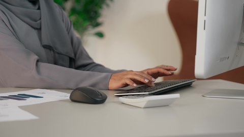 دمج التقنية الحديثة والمتطورة بالحياة العملية، وظيفة مكتبية في شركات الخليج العربي، سيدة سعودية تنجز مهام عملها في المكتب بإيماءات التركيز، تصوير مقرب لامراة عربية خليجية اماراتية ترتدي العباءة تجلس خلف الطاولة تعمل على الحاسب