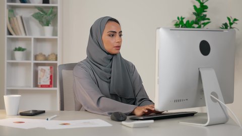 وظيفة مكتبية في شركات الخليج العربي، سيدة سعودية تنجز مهام عملها في المكتب بإيماءات التركيز، استخدام الالة الحاسبة لاجراء العمليات الحسابية، تحليل نتائج البيانات الاحصائية، امراة عربية خليجية اماراتية محجبة ترتدي العباءة تجلس خلف الطاولة تعمل على الحاسب