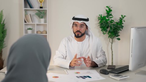 التفاهم والتعاون بين الزملاء ووضع الخطط الاستراتيجية، عقد اجتماع داخل مقر الشركة، موظفان عربيان خليجيان اماراتيان يتعلمان اساليب العمل والتطوير المهني، تبادل الخبرات والمعلومات لتحقيق الاهداف، روح الفريق الواحد والعمل الجماعي، تصوير من الخلف لموظفة محجبة