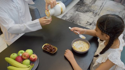 اجواء عائلية سعيدة، تناول وجبة صحية، إفطار صباحي عائلي،  أب عربي خليجي إماراتي يجلس على الطاولة يقوم بصب كوب من القهوه برفقه ابنته، العطف والحنان بين أفراد الأسرة، طفلة خليجيه تقوم بتناول الكورن فليكس بالحليب