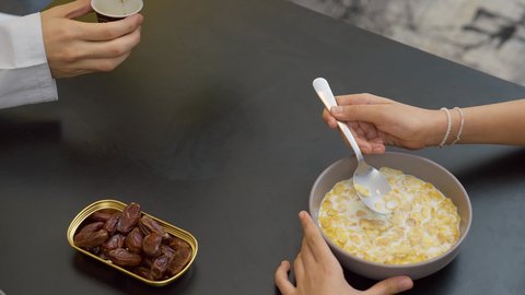 Family breakfast, kindness and tenderness between family members, happy family atmosphere, eating a healthy meal, close-up of an Emirati Gulf Arab father sitting at the table pouring a cup of coffee with his daughter, a Gulf girl eating cornflakes with milk
