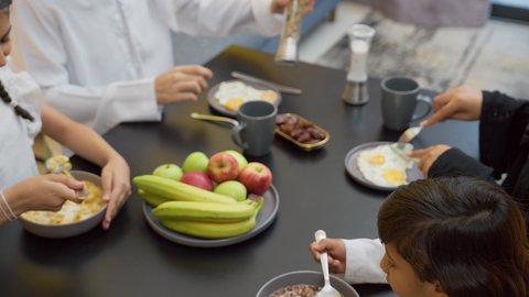 الاستمتاع بتناول المأكولات و المشروبات، وجبة الفطور الصباحية، تدعيم أواصر المحبه والترابط الأسري، عائله عربيه خليجيه اماراتية ترتدي الزي التقليدي يجلسون على الطاوله فى غرفه المعيشه داخل المنزل يقومون بتناول الطعام الصحي