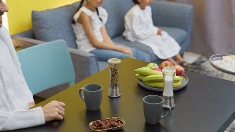 تناول الطعام الصحي، طفلان يجلسان على الأريكة يشاهدان التلفاز، قضاء أوقات ممتعة ومع الأسرة، عائله عربيه خليجيه اماراتية تجلس فى غرفه المعيشه داخل المنزل، رجل عربي خليجي اماراتي يرتدي الكندورة و الغتره يجلس على طاولة الطعام برفقه زوجته يتناولان الافطار