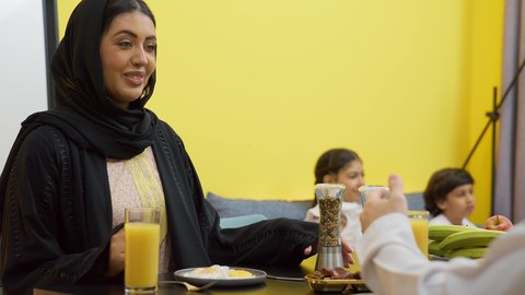 تعزيز الروابط الأسرية، طفلان يجلسان على الأريكة يشاهدان التلفاز، قضاء أوقات ممتعة ومع الأسرة، عائله عربيه خليجيه اماراتية تجلس فى غرفه المعيشه داخل المنزل، رجل عربي خليجي اماراتي يرتدي الكندورة و الغتره يجلس على طاولة الطعام برفقه زوجته يتناولان الافطار