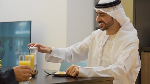 قضاء أوقات ممتعة، تدعيم أواصر المحبه والترابط الأسري، عائله عربيه خليجيه اماراتية تجلس فى غرفه المعيشه داخل المنزل، رجل عربي خليجي اماراتي يرتدي الكندورة و الغتره يجلس على طاولة الطعام برفقه زوجته  يتناولان الافطار