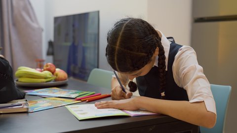 قضاء اوقات عائلية ممتعة في المنزل، عائله عربيه خليجيه اماراتية ترتدي الزي التقليدي يجلسون في غرفه المعيشه مع ابنائهم بأيماءات السعادة و السرور، التعلم والابداع وتنمية المهارات،  تصوير مقرب لفتاة عربيه خليجيه تقوم باداء واجباتها المدرسية