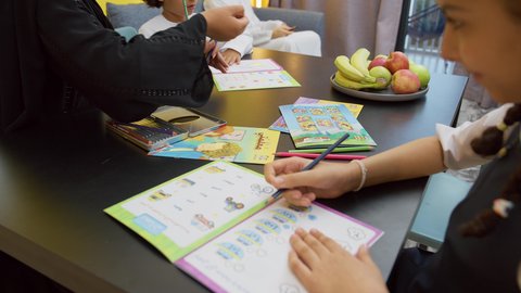 عائله عربيه خليجيه اماراتية ترتدي الزي التقليدي يجلسون في غرفه المعيشه مع ابنائهم بأيماءات السعادة و السرور، التعلم والابداع وتنمية المهارات، قضاء اوقات عائلية ممتعة في المنزل، تصوير مقرب لفتاة عربيه خليجيه تقوم باداء واجباتها المدرسية