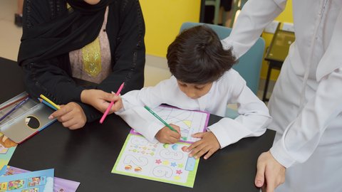 لعبة تلوين الرسومات، الاهتمام بتعليم بالأبناء ودعمهم، الانشطة التعليمية وتنمية القدرات، تصوير علوي لزوجين عربيين خليجيين اماراتيين يرتديان الزي التقليدي يجلسان على الطاولة يقومان بتعليم ابنائهم، استغلال أوقات الفراغ بالأنشطة الترفيهية الممتعة