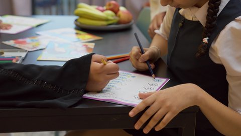 التعلم والابداع وتنمية المهارات، قضاء اوقات عائلية ممتعة في المنزل، عائله عربيه خليجيه اماراتية ترتدي الزي التقليدي يجلسون في غرفه المعيشه مع ابنائهم بأيماءات السعادة و السرور ، تصوير مقرب لفتاة عربيه خليجيه تقوم باداء واجباتها المدرسية