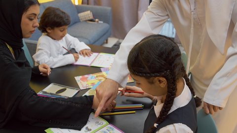 تنمية المهارات الثقافية والقدرات الفكرية للابناء، انشطة ترفيهية فنية ابداعية، لعبة تلوين الرسومات، زوجان عربيان خليجيان اماراتيان يرتديان الزي التقليدي يجلسان على الطاولة يقومان بتعليم ابنائهم، استغلال أوقات الفراغ بالأنشطة الترفيهية الممتعة