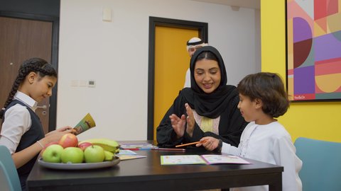 الاهتمام بتعليم الأبناء، الأنشطة التعليمية وتنميه قدرات الابناء بالتعلم، دعم وتشجيع الاطفال لحل الدروس والواجبات المدرسيه المنزليه،عائله عربيه خليجيه اماراتية ترتدي الزي التقليدي تجلس على الطاوله وتساعد ابنائها  في التعليم والقراءه