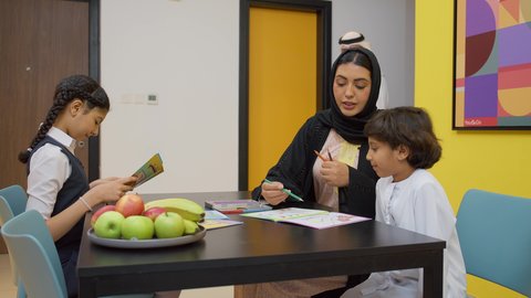الأنشطة التعليمية وتنميه قدرات الابناء بالتعلم، الاهتمام بتعليم الأبناء، دعم وتشجيع الاطفال لحل الدروس والواجبات المدرسيه المنزليه،عائله عربيه خليجيه اماراتية ترتدي الزي التقليدي تجلس على الطاوله وتساعد ابنائها  في التعليم والقراءه