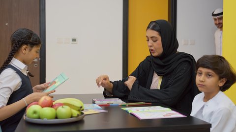 الاهتمام بتعليم الأبناء، الأنشطة التعليمية وتنميه قدرات الابناء بالتعلم، دعم وتشجيع الاطفال لحل الدروس والواجبات المدرسيه المنزليه،عائله عربيه خليجيه اماراتية ترتدي الزي التقليدي تجلس على الطاوله وتساعد ابنائها  في التعليم والقراءه