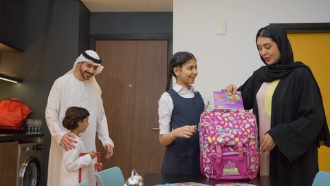 البهجة بالعودة إلى المدرسة, بداية عام دراسي جديد، ام خليجيه ترتدي العباءه السوداء تقوم بوضع الكتب و الدفاتر داخل الحقيبة المدرسية برفقه ابنتها, أجواء صباحية عائلية داخل المنزل، رجل عربي خليجي إماراتي يرتدي الكندورة والغترة يستعد للنزول مع اولاده