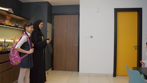 استقبال العام الدراسي الجديد بحماس، أجواء صباحية عائلية داخل المنزل، رجل عربي خليجي إماراتي يرتدي الكندورة والغترة يستعد للنزول مع اولادة، ام عربيه خليجيه اماراتية ترتدي العباءه تقوم بتوديع ابنائها عند الذهاب إلى المدرسة