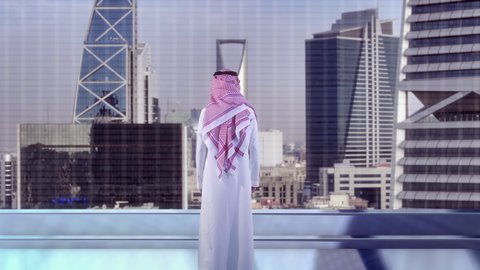 المباني والمنشآت الاقتصادية المالية, الأبراج وناطحات السحاب السكنية والتجارية، رؤية مستقبلية 2030، تصوير من الخلف لرجل عربي خليجي سعودي يرتدي الثوب والشماغ التقليدي يقف أمام المعالم السياحية المشهورة المضاءة باللون الأزق، النمو والتطور العمراني في المملكة