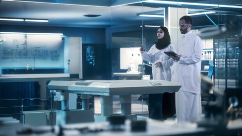 طبيب عربي خليجي سعودي يرتدي المعطف الأبيض يقف مع طبيبة في غرفة طبية مجهزة بالأدوات والشاشات الرقمية للتشخيص وشرح الحالات المرضية، مجسم هولوجرامي ثلاثي الابعاد لدماغ الانسان، التطور والتقدم في المجال الطبي المستقبلي في المملكة