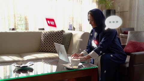 رموز التعبير عن الحب، مجموعة من اشعارات السوشال ميديا، سيدة عربية خليجية سعودية محجبة ترتدي عباءة تقوم باستخدام جهاز الحاسوب المحمول بإيماءات السرور والسعادة، فقاعات مواقع التواصل الإجتماعي والتطبيقات، تناول القهوة الساخنة