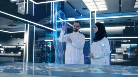 طبيب عربي خليجي سعودي يرتدي المعطف الأبيض يقف مع طبيبة في غرفة طبية مجهزة بالأدوات والشاشات الرقمية للتشخيص وشرح الحالات المرضية،  مجسم هولوجرامي ثلاثي الابعاد لهيكل جسم الانسان، التطور والتقدم في المجال الطبي المستقبلي في المملكة