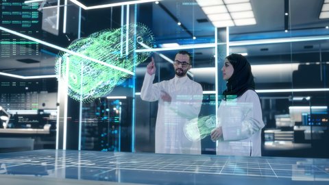 مفهوم الهندسة الطبية، طبيب عربي خليجي سعودي يرتدي المعطف الأبيض يقف مع طبيبة في غرفة طبية مجهزة بالأدوات والشاشات الرقمية للتشخيص والعلاج الطبي،  شاشة مضيئة تعرض مجسم هولوجرامي ثلاثي الابعاد للآلات الطبية، التطور والتقدم في المجال الطبي المستقبلي في المملكة