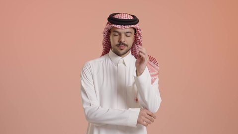 تعابير وجه ويدين تدل على الملل والكآبة، إيماءات التفكير والتأمل، الوقوف باستقامة والنظر إلى الكاميرا، بورتريه لشاب عربي سعودي خليجي يرتدي الثوب التقليدي و الشماغ يضع يده على وجهه