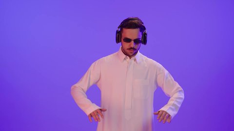 الاستمتاع بتقنية الهيدفون، استخدام الأجهزة التكنولوجية، إيماءات الاندماج والتركيز عند الاستماع إلى الموسيقا والمقاطع الصوتية، بورتريه لشاب عربي خليجي سعودي يرتدي الثوب التقليدي يضع نظارة الشمسية و سماعة الرأس و يقوم بالرقص