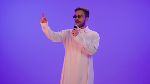 أداء أمام جمهور, بورتريه لرجل عربي خليجي سعودي سعيد يرتدي الثوب التقليدي و نظارة شمسية، يحمل الميكروفون و يغني بحماس، ايماءات وجه و يدين تدل على السعادة و الاستمتاع, ممارسة موهبة الغناء