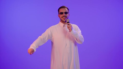 ممارسة موهبة الغناء، الاستمتاع بأداء المواهب الصوتية، بورتريه لشاب عربي خليجي سعودي يرتدي الزي التقليدي ونظارة شمسية  يمسك بيده المايكروفون ويغني بحماس بإيماءات تدل على الاندماج والتفاعل، تسجيل مقطع صوتي غنائي