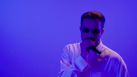 الاستمتاع بأداء المواهب الصوتية، بورتريه لرجل عربي خليجي سعودي سعيد يرتدي الزي التقليدي و نظارة شمسية، يحمل الميكروفون و يغني بحماس، ايماءات وجه و يدين تدل على السعادة و الاستمتاع, ممارسة موهبة الغناء