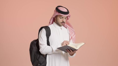 مراجعة الدروس اليومية, القراءة بتمعن و تركيز، بورتريه لطالب جامعي عربي خليجي سعودي يرتدي الثوب التقليدي والشماغ يضع الحقيبة على ظهره و يحمل بيده كتاب جامعي