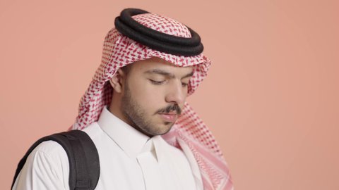 القراءة بتمعن و تركيز، بورتريه لطالب جامعي عربي خليجي سعودي يرتدي الثوب التقليدي والشماغ  يضع الحقيبة على ظهره و يحمل بيده كتاب جامعي، مراجعة الدروس اليومية