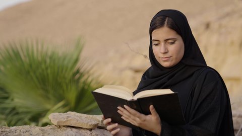 بناء المعرفة عبر القراءة والاطلاع الذاتي، الأنشطة الترفيهية الثقافية، الشغف بممارسة الهوايات المفيدة, تصوير مقرب لإمرأة عربية خليجية سعودية ترتدي العباءة والحجاب تقوم بالقراءة والمطالعة في الهواء الطلق