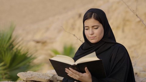 مفهوم التعلم الذاتي واكتساب المعرفة، الأنشطة الترفيهية الثقافية، الشغف بممارسة الهوايات المفيدة, تصوير مقرب لإمرأة عربية خليجية سعودية ترتدي العباءة والحجاب تقوم بالقراءة والمطالعة في الهواء الطلق