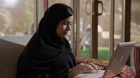 Content creation, typing on the keyboard, the concept of data entry, a side view of a Saudi Gulf Arab woman sitting in the living room using a laptop, typing on the laptop, integrating modern technology into practical life.