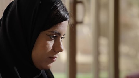 تركيز وتأمل عميق، تصوير مقرب من الجانب لامرأة عربية خليجية سعودية ترتدي الحجاب و العباءة تنظر للأسفل داخل غرفة مضاءة بضوء الشمس