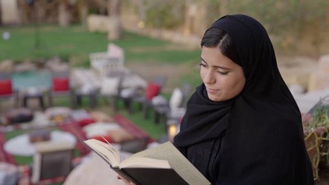 الشغف بممارسة الهوايات المفيدة، مفهوم الثقافة والاطلاع والتعلم الذاتي, تصوير مقرب لإمرأة عربية خليجية سعودية ترتدي العباءة والحجاب تقوم بالقراءة والمطالعة في الهواء الطلق, الأنشطة الترفيهية الثقافية