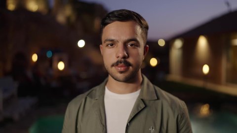 النظر الى الكاميرا بتعابير السرور والبشاشة،  شاب عربي خليجي سعودي يرتدي الزي الكاجوال يقف في الهواء الطلق ،  مفهوم الرجولة والوسامة، الاهتمام بالمظهر الخارجي والأناقة، الوقوف بأيدي متقاطعة بإيماءات الثقة بالنفس