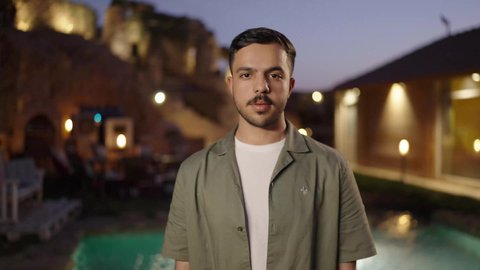 مفهوم الرجولة والوسامة، الاهتمام بالمظهر الخارجي والأناقة، الوقوف بأيدي متقاطعة بإيماءات الثقة بالنفس، شاب عربي خليجي سعودي يرتدي الزي الكاجوال يقف في الهواء الطلق و ينظر الى الكاميرا بتعابير السرور والبشاشة