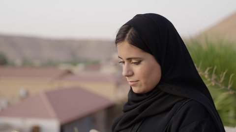 الأنشطة الترفيهية الثقافية، الشغف بممارسة الهوايات المفيدة، مفهوم الثقافة والاطلاع والتعلم الذاتي, تصوير مقرب لإمرأة عربية خليجية سعودية ترتدي العباءة والحجاب تقوم بالقراءة والمطالعة في الهواء الطلق