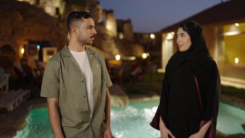 النظر الي الكاميرا بايماءات السعادة و السرور ، الأناقة والاهتمام بالمظهر الخارجي،  تعابير الثقة بالنفس ، زوجان عربيان خليجيان سعوديان يقفان بإستقامة بإيدي متقاطعة فى الهواء الطلق