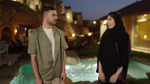 الأناقة والاهتمام بالمظهر الخارجي، النظر الي الكاميرا بايماءات السعادة و السرور ،  ايماءات الثقة بالنفس ، زوجان عربيان خليجيان سعوديان يقفان بإستقامة بإيدي متقاطعة فى الهواء الطلق